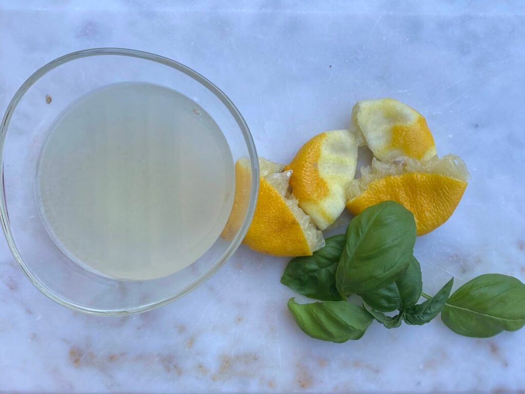 Freshly squeezed lemon juice in a glass bowl next to the squeezed lemon halves and fresh basil leaves