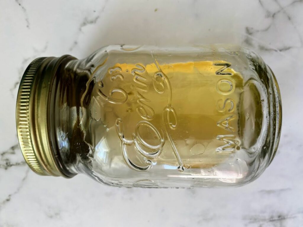 lemon basil simple syrup in a mason jar on a white marble counter