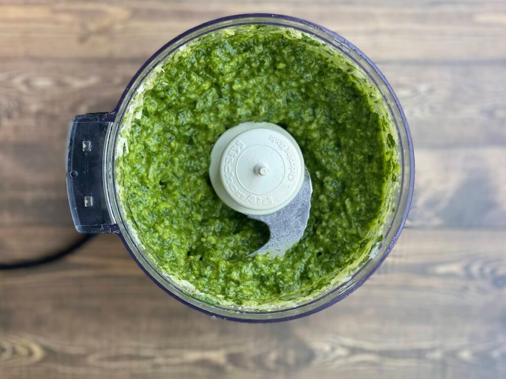 Tuscany basil pesto after being blended in the food processor. You can throw tender young basil stems into pesto, and basil flowers and flower buds.