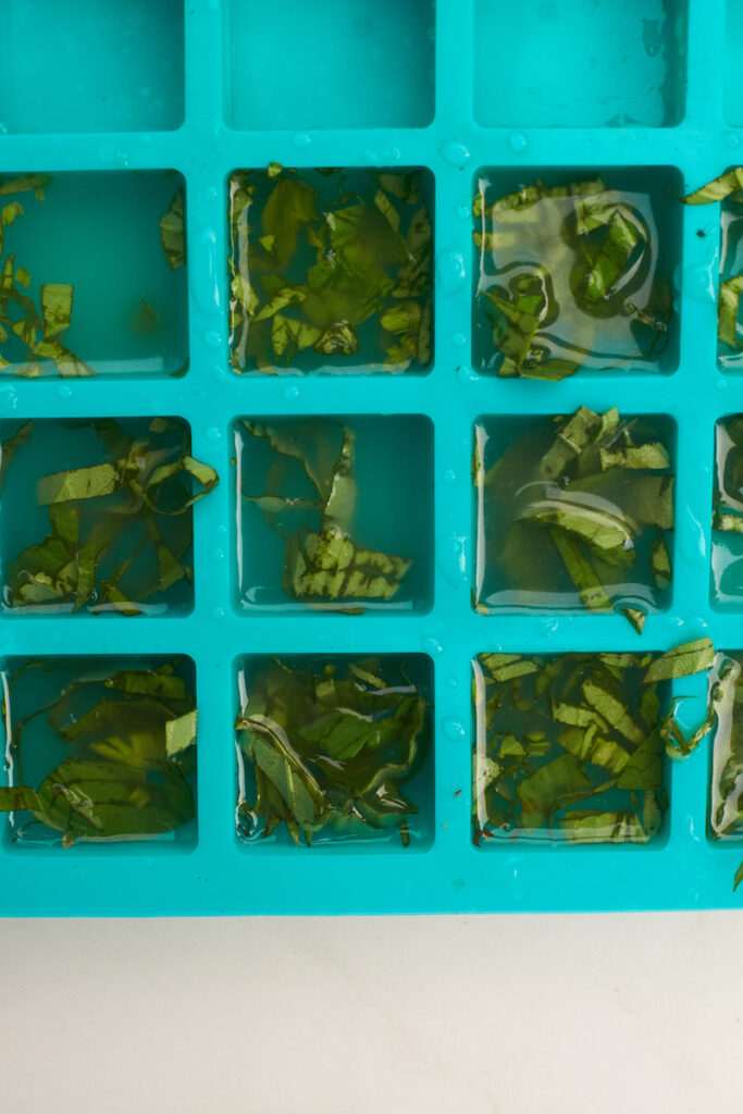 Silicone ice cube tray filled with basil ribbons and chicken broth before freezing