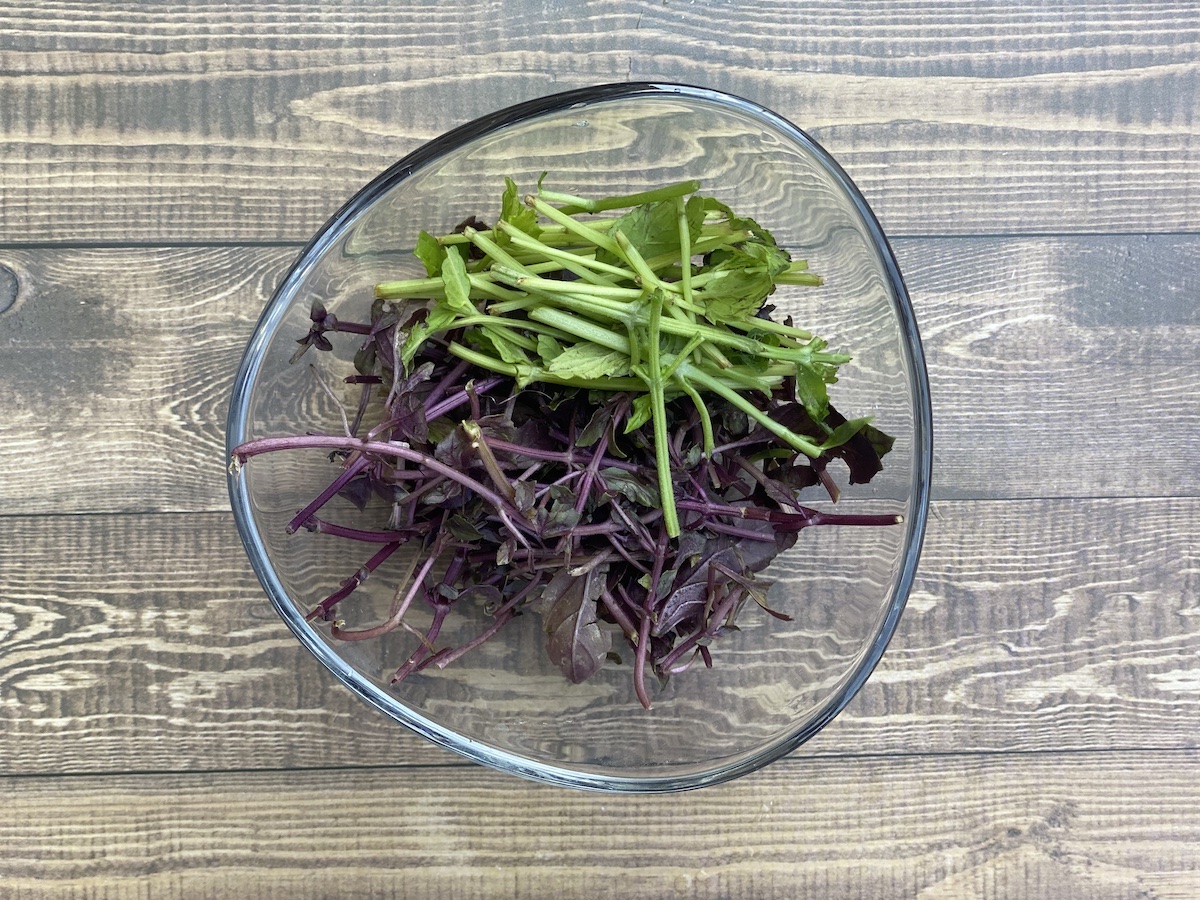 tender young green and purple basil stems in a clear glass bowl against a wood plank background