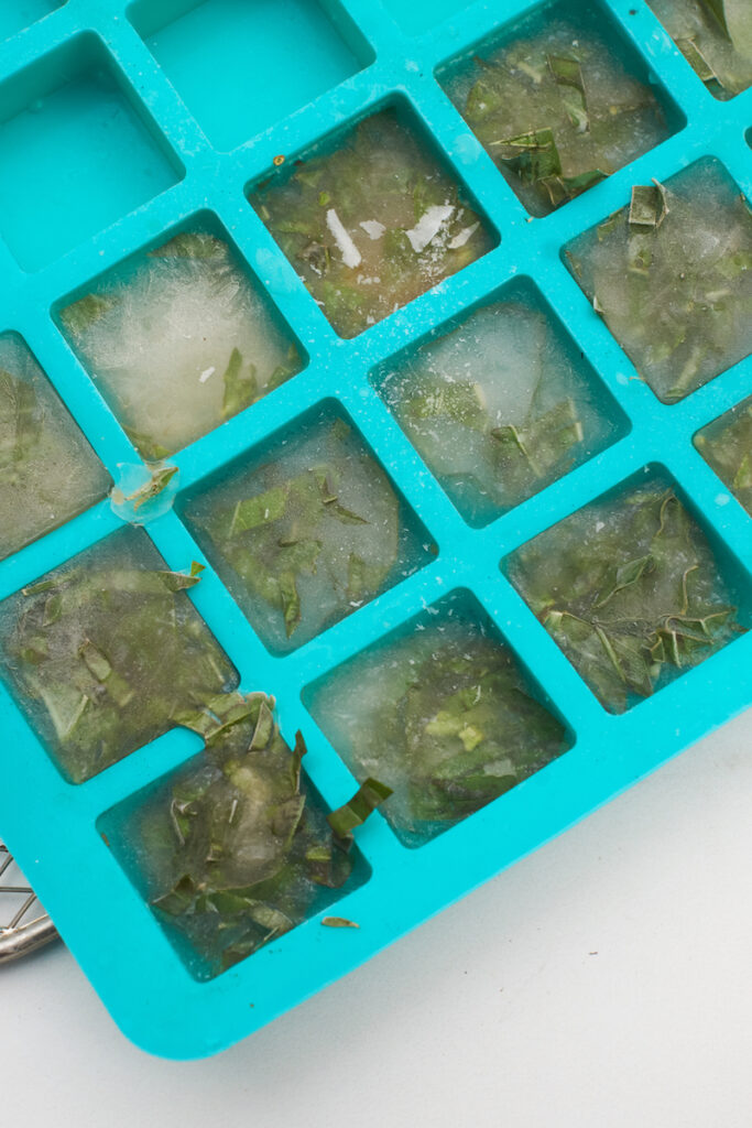 Frozen cubes of basil ribbons and broth in an ice cube tray after removing from freezer