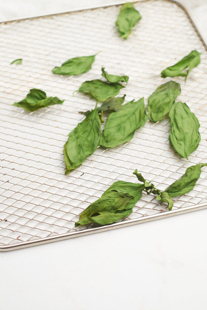 Basil leaves in an air fryer basket. The leaves are fully dry after 3 minutes of drying basil in air fryer.