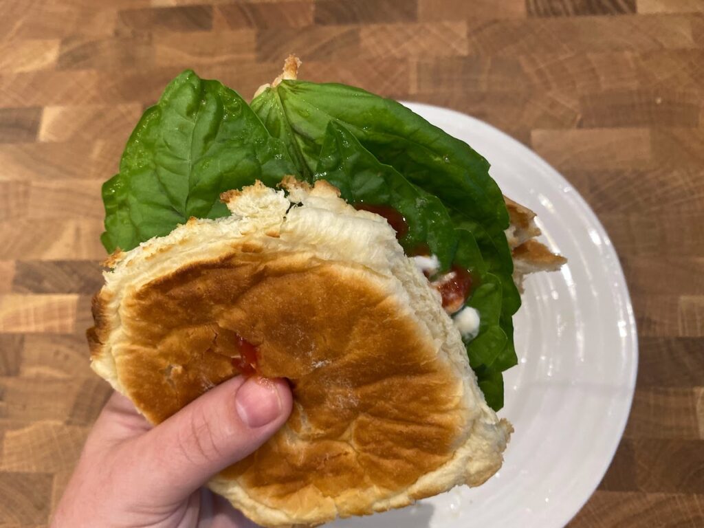 lettuce leaf basil leaves in a homemade hamburger. A woman's hand holds the burger over a white plate sitting on butcher block